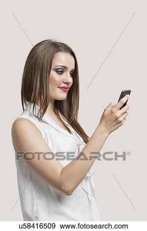 Stock Photo - Beautiful young woman using cell phone against gray background. Fotosearch