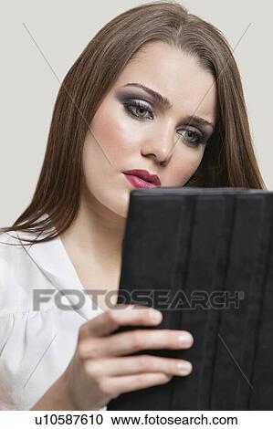 Stock Image - Beautiful young woman using tablet PC over gray background. Fotosearch