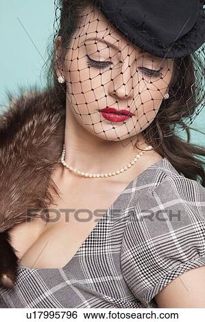 Stock Photograph - Beautiful young woman with veiled hat and fur boa against blue background. Fotosearch