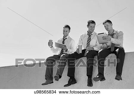 Picture - Black and white photo of thoughtful businessmen sitting while using digita tablet in office rooftop . Fotosearch