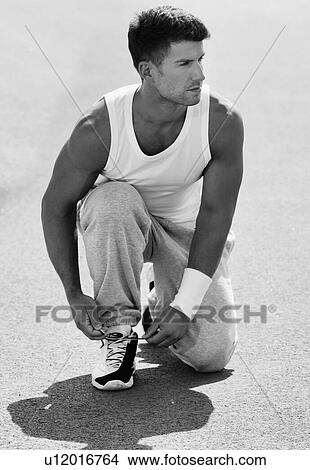 Black and white photo of young attractive man wearing sports wear tying his rubber shoes in park View Large Photo Image Picture - Black and white photo of young attractive man wearing sports wear tying his rubber shoes in park. Fotosearch
