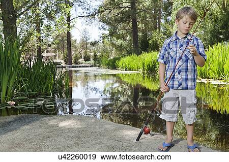 Stock Photo - Boy adjusting fishing rod's line while standing by lake. Fotosearch