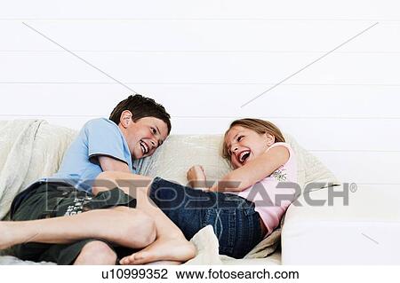 Stock Image - Brother and sister relaxing on sofa together. Fotosearch