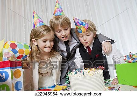 Brothers and sister wearing party hat looking at birthday cake together View Large Photo Image Picture - Brothers and sister wearing party hat looking at birthday cake together. Fotosearch