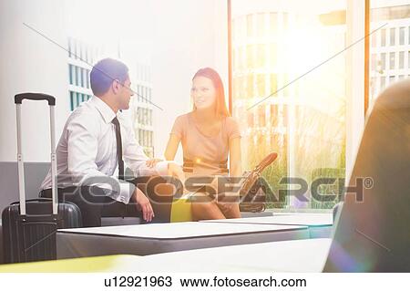 Stock Image - Business couple talking while sitting and waiting in hotel reception area. Fotosearch