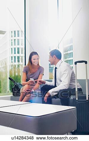Stock Photo - Business couple talking while sitting and waiting in hotel reception area. Fotosearch