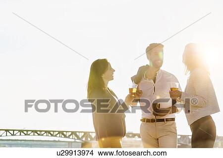 Picture - Business people celebrating success while drinking beer on the beach with lens flare in background. Fotosearch