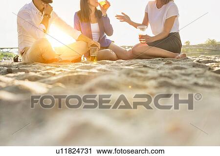 Stock Image - Business people celebrating success while drinking beer on the beach with lens flare in background. Fotosearch