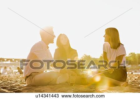 Stock Image - Business people celebrating success while drinking beer on the beach with lens flare in background. Fotosearch
