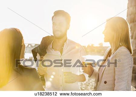 Stock Image - Business people celebrating success while drinking beer on the beach with lens flare in background. Fotosearch