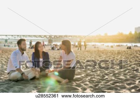 Stock Image - Business people celebrating success while drinking beer on the beach with lens flare in background. Fotosearch
