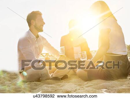 Stock Image - Business people celebrating success while drinking beer on the beach with lens flare in background. Fotosearch