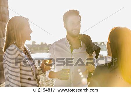 Stock Photo - Business people celebrating success while drinking beer on the beach with lens flare in background. Fotosearch