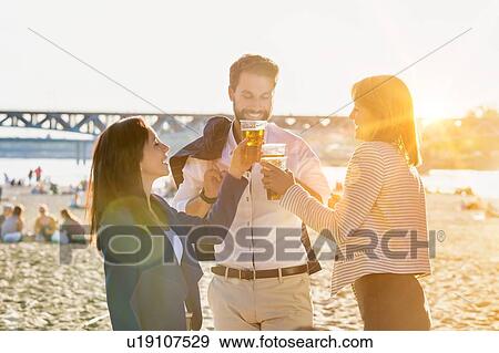 Stock Photo - Business people celebrating success while drinking beer on the beach with lens flare in background. Fotosearch
