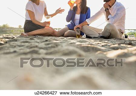 Stock Photo - Business people celebrating success while drinking beer on the beach with lens flare in background. Fotosearch