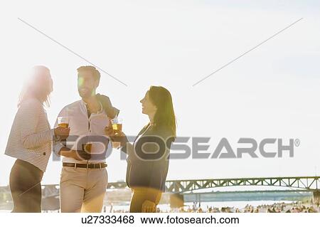 Stock Photo - Business people celebrating success while drinking beer on the beach with lens flare in background. Fotosearch