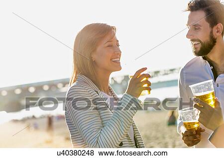 Stock Photo - Business people celebrating success while drinking beer on the beach with lens flare in background. Fotosearch