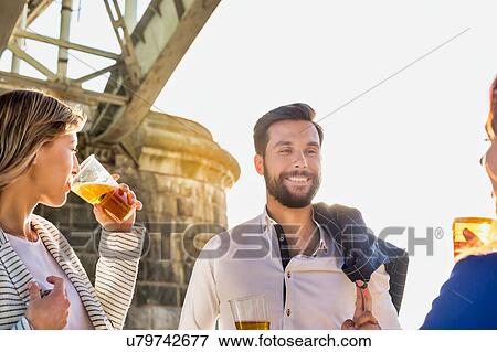 Stock Photo - Business people celebrating success while drinking beer on the beach with lens flare in background. Fotosearch