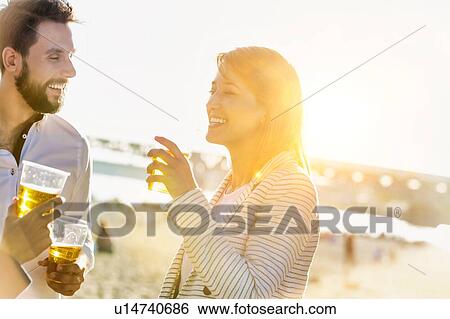 Stock Photograph - Business people celebrating success while drinking beer on the beach with lens flare in background. Fotosearch
