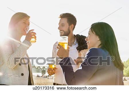 Stock Photograph - Business people celebrating success while drinking beer on the beach with lens flare in background. Fotosearch