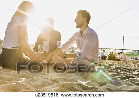 Stock Photograph - Business people celebrating success while drinking beer on the beach with lens flare in background. Fotosearch