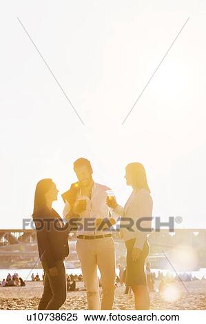 Stock Photography - Business people celebrating success while drinking beer on the beach with lens flare in background. Fotosearch