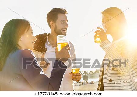 Stock Photography - Business people celebrating success while drinking beer on the beach with lens flare in background. Fotosearch