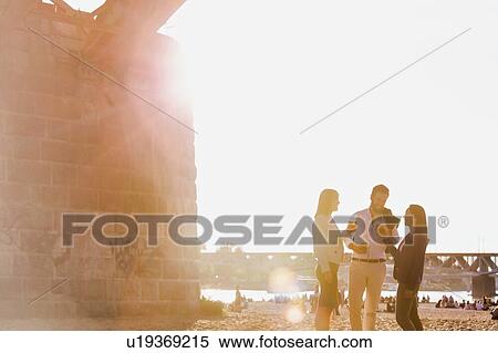 Stock Photography - Business people celebrating success while drinking beer on the beach with lens flare in background. Fotosearch