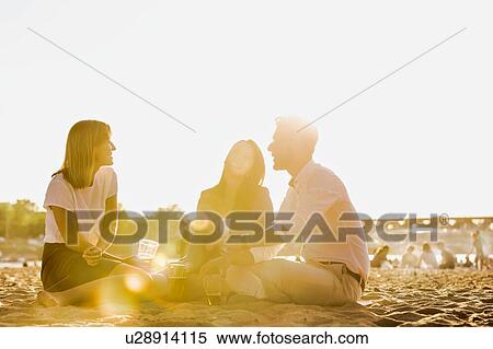 Stock Photography - Business people celebrating success while drinking beer on the beach with lens flare in background. Fotosearch