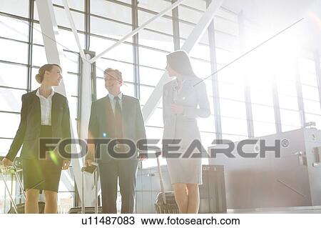 Stock Image - Business people discussing plans while walking with their luggage in airport. Fotosearch