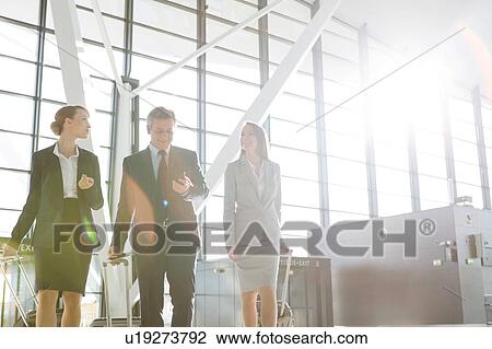 Business people discussing plans while walking with their luggage in airport View Large Photo Image Stock Image - Business people discussing plans while walking with their luggage in airport. Fotosearch