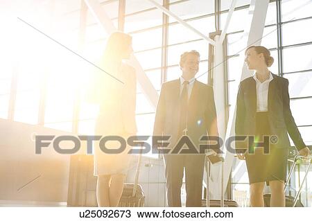 Stock Image - Business people discussing plans while walking with their luggage in airport. Fotosearch