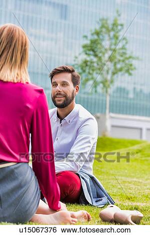 Stock Photograph - Business people discussing plans while sitting on the grass outdoor. Fotosearch