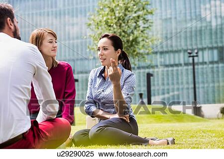 Stock Photography - Business people discussing plans while sitting on the grass outdoor. Fotosearch