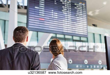 Stock Photo - Business people looking on flight display screen in airport. Fotosearch