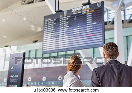 Stock Photograph - Business people looking on flight display screen in airport. Fotosearch