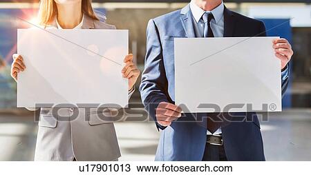 Stock Image - Business people standing while holding blank white placard in arrival area at airport . Fotosearch