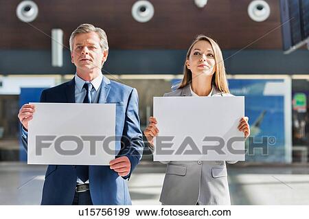 Business people standing while holding blank white placard in arrival area at airport  View Large Photo Image Stock Photo - Business people standing while holding blank white placard in arrival area at airport . Fotosearch