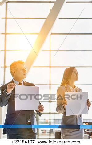 Stock Photo - Business people waiting while holding blank white placard in arrival area at airport . Fotosearch