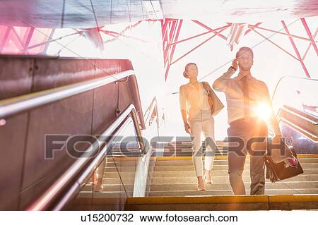 Stock Image - Business people walking downstairs with lens flare in background. Fotosearch