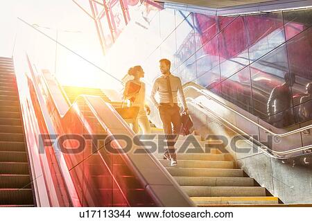 Businessman and businesswoman talking while walking down stairs with lens flare in background View Large Photo Image Picture - Businessman and businesswoman talking while walking down stairs with lens flare in background. Fotosearch