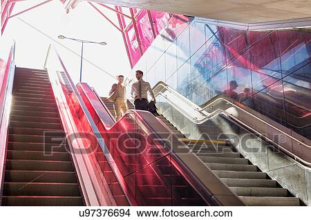 Businessman and businesswoman talking while walking down stairs with lens flare in background View Large Photo Image Picture - Businessman and businesswoman talking while walking down stairs with lens flare in background. Fotosearch