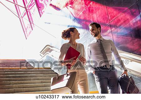 Businessman and businesswoman talking while walking down stairs with lens flare in background View Large Photo Image Stock Photo - Businessman and businesswoman talking while walking down stairs with lens flare in background. Fotosearch