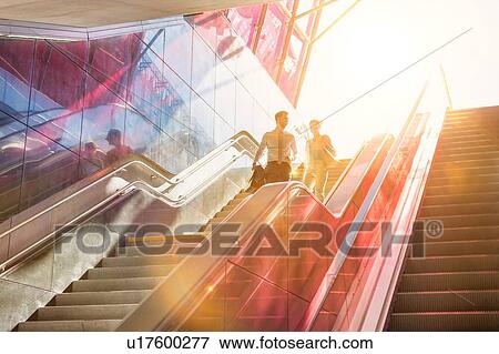 Businessman and businesswoman talking while walking down stairs with lens flare in background View Large Photo Image Stock Photo - Businessman and businesswoman talking while walking down stairs with lens flare in background. Fotosearch