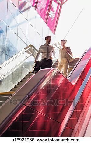 Businessman and businesswoman talking while walking down stairs with lens flare in background View Large Photo Image Stock Photograph - Businessman and businesswoman talking while walking down stairs with lens flare in background. Fotosearch
