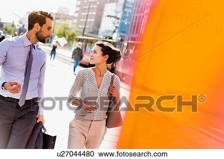 Stock Image - Businessman and businesswoman walking while discussing plans before meeting. Fotosearch