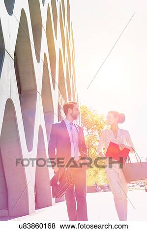 Stock Photo - Businessman and businesswoman walking while discussing plans before meeting. Fotosearch