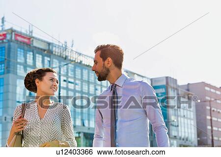 Stock Photograph - Businessman and businesswoman walking while discussing plans before meeting. Fotosearch