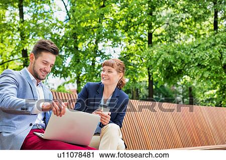 Businessman discussing plans over laptop with beautiful businesswoman while sitting on bench View Large Photo Image Stock Image - Businessman discussing plans over laptop with beautiful businesswoman while sitting on bench. Fotosearch