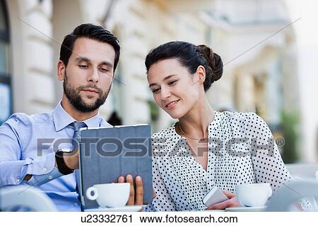 Stock Image - Businessman discussing plans over digital tablet to businesswoman while sitting and waiting for their food at restaurant. Fotosearch